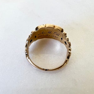 May include: A gold ring with an intricate design and inscription. The inscription reads "A.M.B. 28th Feb 1855".