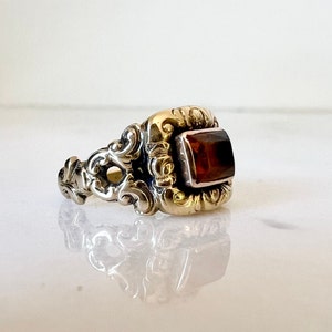 May include: A gold ring with an ornate design and a rectangular brown gemstone.