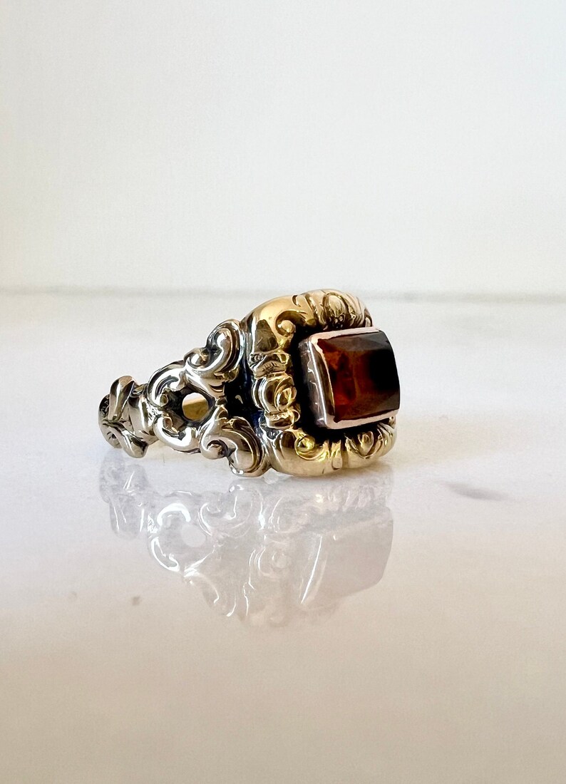 May include: A gold ring with an ornate design and a rectangular brown gemstone.