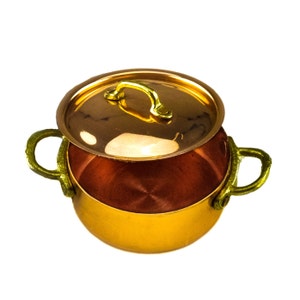 May include: A small copper pot with a lid and gold handles. The pot is empty and the lid is slightly ajar.