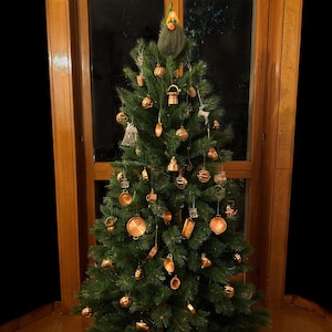 May include: A Christmas tree adorned with copper-coloured kitchen utensil ornaments and miniature cookware. The tree stands before a window with wooden frames, and a whimsical gnome sits atop.