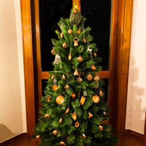 Puede incluir: Un árbol de Navidad verde decorado con adornos de color cobre, incluyendo campanas, estrellas y otras formas. El árbol está decorado con un gnomo en la parte superior.