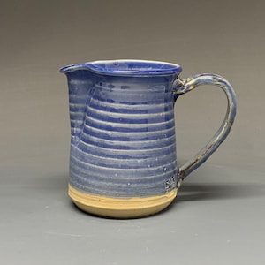 May include: A blue and white striped ceramic pitcher with a brown handle. The pitcher has a light brown base.