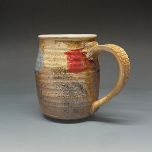 May include: A handmade ceramic mug with a brown, red, and blue glaze. The mug has a unique, textured handle.