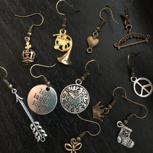 May include: Assortment of silver and gold tone earrings with various charms, including a crown, a musical instrument, a heart, a hanger, a clock, a peace sign, an arrow, a stocking, a bow, and a charm with the words "live laugh love".