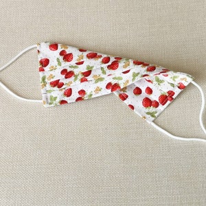 May include: A white face mask with a red strawberry print and white elastic straps.