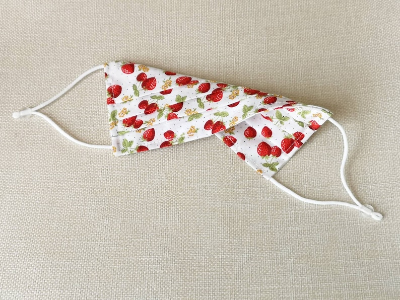 May include: A white face mask with a red strawberry print and white elastic straps.