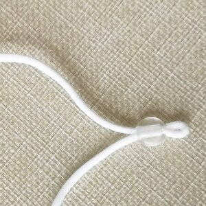 May include: White elastic cord with a clear plastic slider. The cord is looped through the slider and tied off.