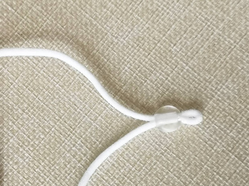 May include: White elastic cord with a clear plastic slider. The cord is looped through the slider and tied off.