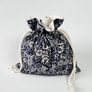 May include: A small, drawstring bag made of navy blue fabric with a white floral pattern. The bag has a white cotton lining and white cotton drawstrings.