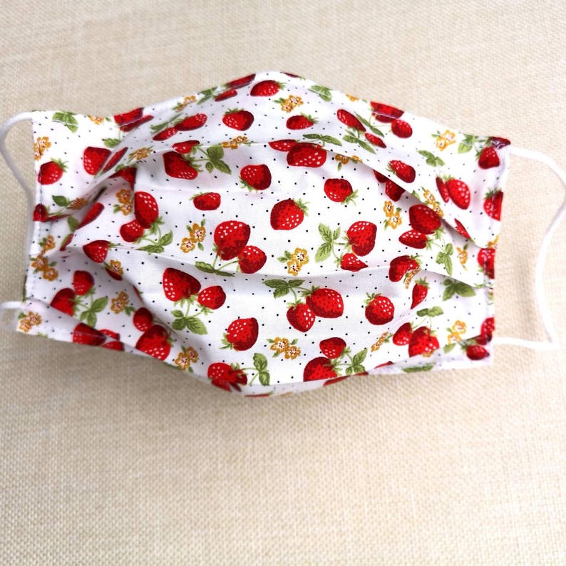 May include: White face mask with a red strawberry print. The mask has white polka dots and green leaves on the strawberries.