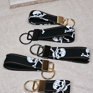 May include: Four black keychains with gold rings and a skull and crossbones pattern. The keychains are made of fabric and have a white skull and crossbones design.