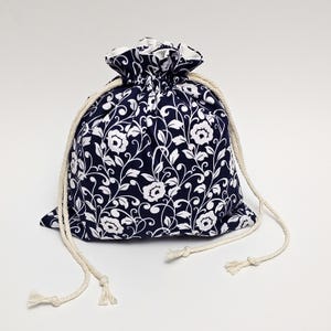May include: A navy blue drawstring bag with a white floral pattern. The bag has white cotton drawstrings.