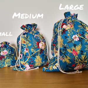 May include: Three drawstring bags in different sizes, labelled "Small", "Medium", and "Large". The bags are made of a teal fabric with a floral pattern and white drawstrings.