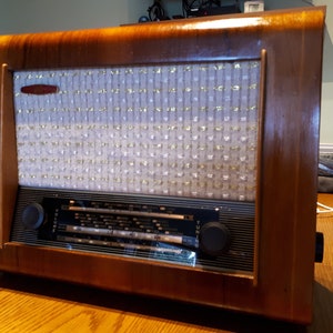 May include: A vintage wooden radio with a white cloth speaker grille and black tuning knobs. The radio has a volume knob labelled "Volume" and a tuning knob labelled "Tuning".