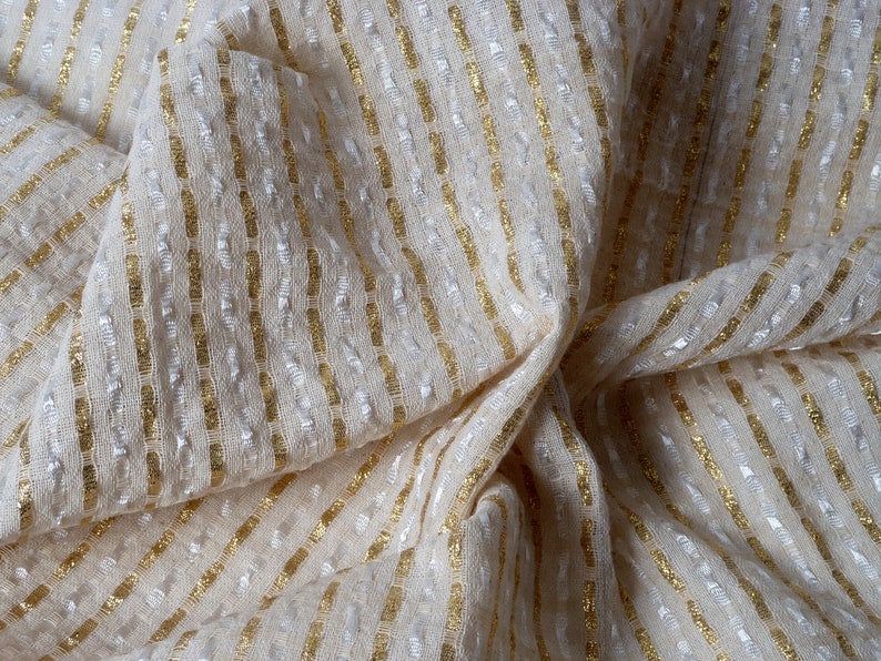 May include: White fabric with gold stripes. The fabric is textured and has a subtle sheen.