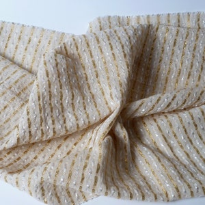 May include: A beige fabric with gold and silver stripes. The fabric has a textured surface and is woven with a subtle shimmer.
