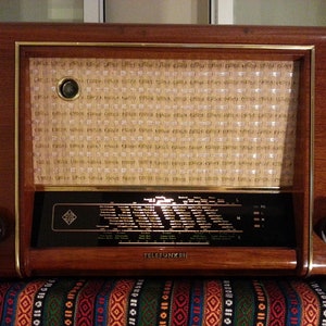 May include: A vintage wooden radio with a gold trim and a speaker grille. The radio has a black dial with a white label that reads "TELEFUNKEN".