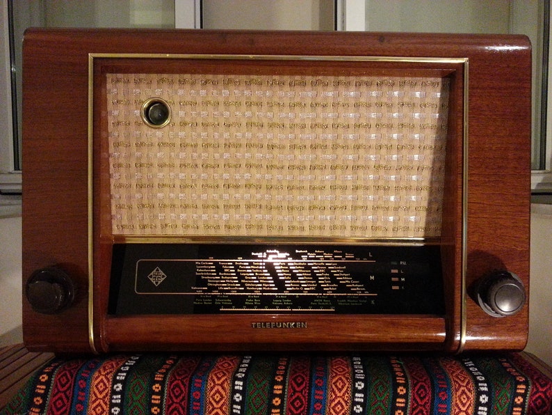 May include: A vintage wooden radio with a gold trim and a speaker grille. The radio has a black dial with a white label that reads "TELEFUNKEN".