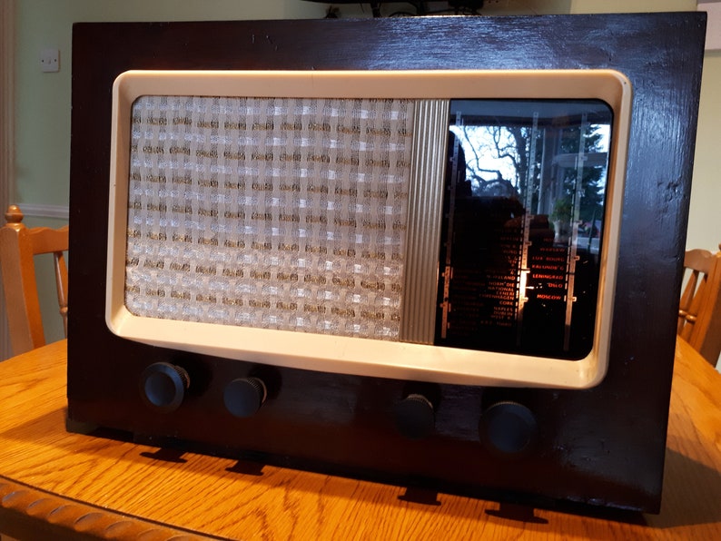 May include: A vintage wooden radio with a white face and black knobs. The radio has a speaker grille and a glass window that shows the inner workings of the radio.