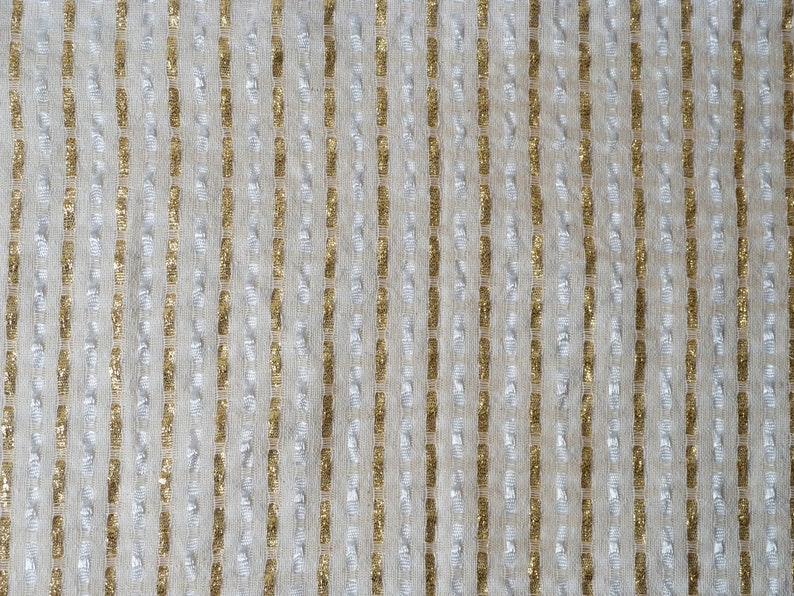 May include: A close-up of a textured fabric with vertical stripes of gold and silver thread.