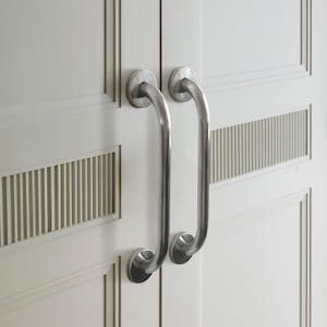 Può includere: Due maniglie per porte argentate con bordi arrotondati e una finitura liscia. Le maniglie sono montate su una porta bianca con un pannello decorativo.