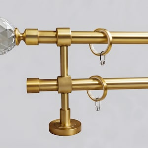 Puede incluir: Barra de cortina doble dorada con terminales de cristal. La barra está montada en la pared con un soporte decorativo. La barra está diseñada para sujetar dos juegos de cortinas.