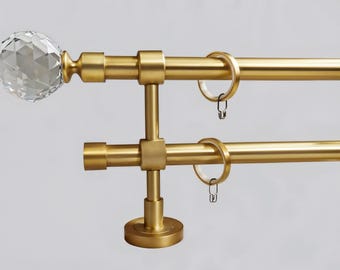 May include: Gold double curtain rod with crystal finials. The rod is mounted to the wall with a decorative bracket. The rod is designed to hold two sets of curtains.