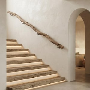 Könnte beinhalten: Eine Treppe mit dicken, verwitterten Holzstufen und integrierter Beleuchtung unter den Stufen. Ein langer, natürlich geformter Ast dient als Handlauf und ist mit einfachen Metallhalterungen an der cremeweißen Wand befestigt.