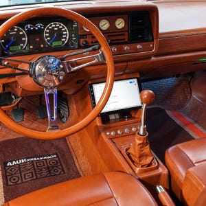 Könnte beinhalten: Das Interieur eines Autos mit braunen Ledersitzen, einem braunen Holzarmaturenbrett und einem braunen Lenkrad. Das Auto verfügt über ein individuelles Soundsystem mit einem bunten Lautsprecher und einem digitalen Display.