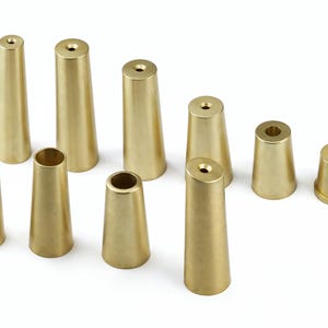 May include: A set of ten brass furniture leg extenders in various sizes. The extenders are cone-shaped and have a smooth, polished finish.