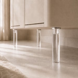 May include: A beige cabinet featuring a smooth, matte finish and rounded corners. The cabinet is supported by three visible, cylindrical, transparent acrylic legs that are attached to the base with silver-toned metal hardware connectors.