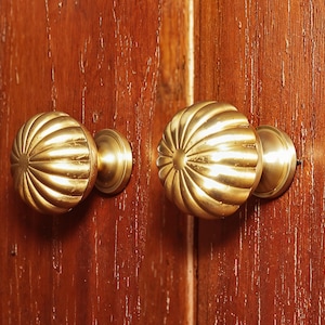 Puede incluir: Dos pomos de armario dorados con un diseño acanalado. Los pomos están montados en una superficie de madera.