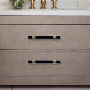 May include: A light gray bathroom vanity with two drawers. The drawers have black and gold handles.