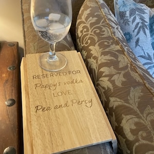 May include: A wooden tray with the text "RESERVED FOR Pappy's vodka LOVE Pea and Percy" engraved on it. The tray is sitting on a sofa with a glass of water and ice on top of it.