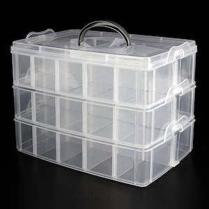 May include: A clear plastic three-tiered storage box with a black handle on the lid. The box has 18 individual compartments.
