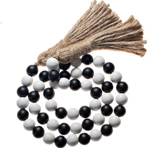 May include: A black and white wooden bead garland with a brown jute tassel. The garland is made of round wooden beads that are painted black and white.