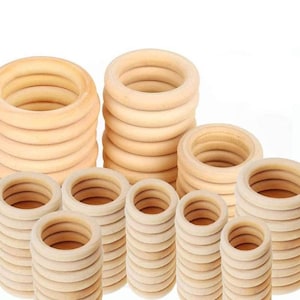 May include: Stacks of unfinished wooden rings in various sizes. The rings are light brown and appear to be made of natural wood. The image shows several stacks of rings, suggesting they are available in bulk.