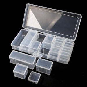 May include: A clear plastic storage box with a hinged lid and multiple compartments of varying sizes. The box is open and the lid is propped up, revealing the compartments inside. The box is ideal for organizing small items like beads, buttons, or jewelry.