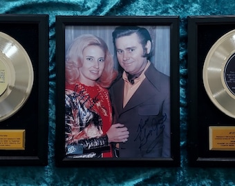 May include: Three gold records framed in black wood frames. The records are for the songs "Beauty Is More Than Skin Deep", "If You're Gonna Do Me Wrong (Do It Right)", and "At Sixteen You're a Sweetheart (But At Seventeen You're a Heartbreaker)". The records are signed by Tammy Wynette and George Jones.