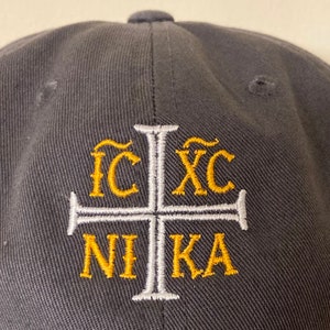May include: A black baseball cap with a white cross and gold lettering that reads "IC XC NIKA".
