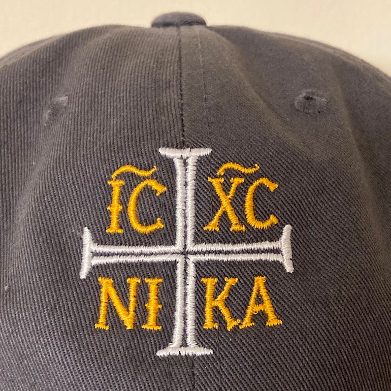 May include: A black baseball cap with a white cross and gold lettering that reads "IC XC NIKA".