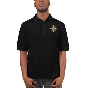 May include: Black polo shirt with a silver cross embroidered on the chest. The cross has the text "IC XC NIKA" in gold lettering.