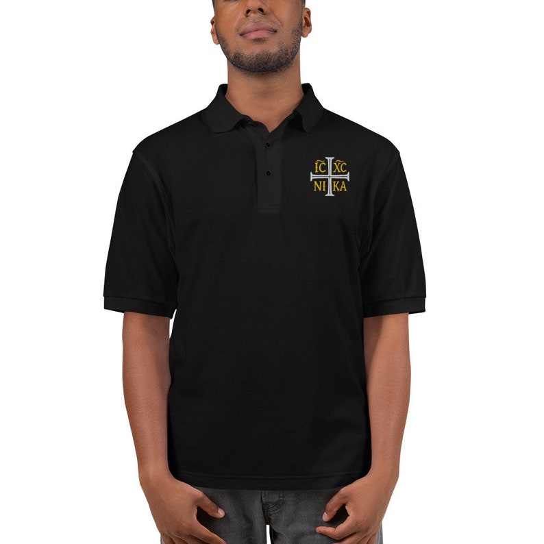 May include: Black polo shirt with a silver cross embroidered on the chest. The cross has the text "IC XC NIKA" in gold lettering.