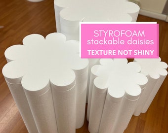 May include: Three white styrofoam daisy-shaped platforms stacked on top of each other. The platforms are textured and not shiny. The text "STYROFOAM stackable daisies TEXTURE NOT SHINY" is printed on a pink background.