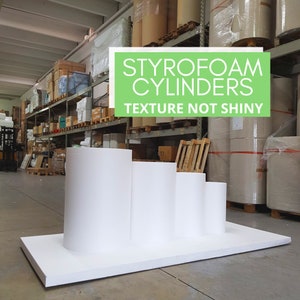 Può includere: Quattro cilindri in polistirolo bianco di diverse dimensioni, disposti in fila su una base in polistirolo bianco. I cilindri hanno una superficie testurizzata, non lucida. Il testo "STYROFOAM CYLINDERS TEXTURE NOT SHINY" è visualizzato sopra i cilindri.