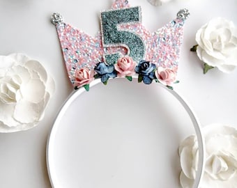 May include: A pink and silver glitter crown headband with a blue and green number 5 and pink and blue flowers.