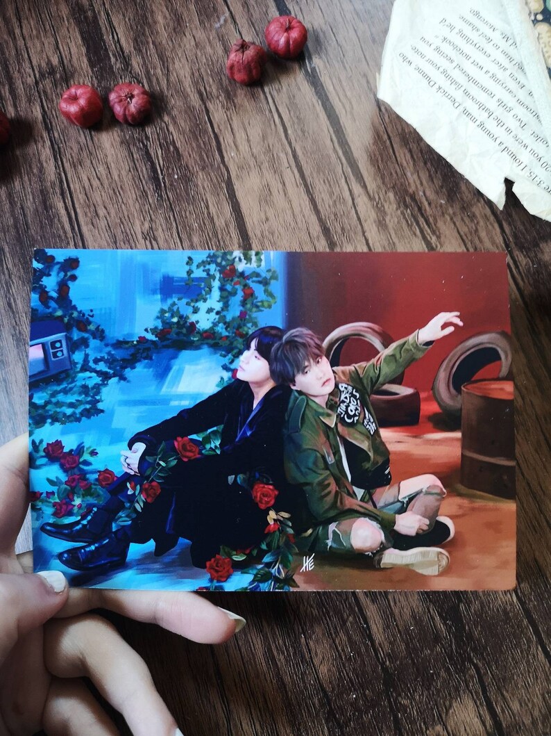 May include: A painting of two people sitting on a floor with a blue and red background. The person on the left is wearing a black outfit and the person on the right is wearing a green jacket and jeans. There are red roses in the foreground.