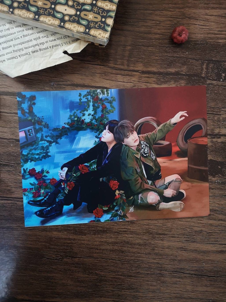 May include: Two men are sitting together in a room with a blue and red background. One man is wearing a black suit and the other is wearing a green jacket. There are red roses in the foreground.