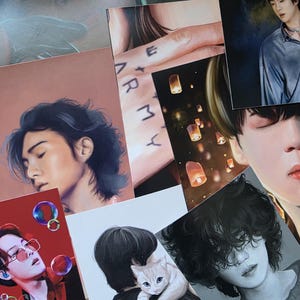 Pode incluir: Uma coleção de impressões artísticas com retratos de pessoas. As impressões apresentam vários estilos, incluindo ilustrações e pinturas. Algumas impressões têm texto, e a paleta de cores inclui vermelhos, azuis e tons neutros. As impressões estão numa superfície de cor clara.